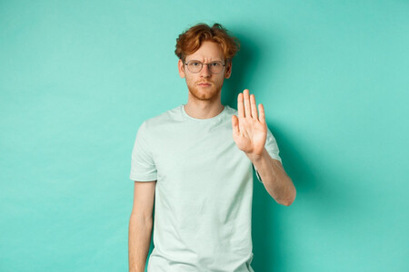 Hombre pelirrojo con gafas sobre fondo verde, levantando la mano para poner límites y negarse